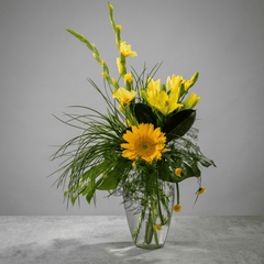 Bouquet of yellow flowers in a clear vase on a gray background